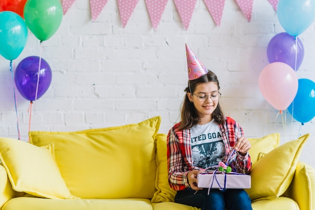 Free photo girl sitting on sofa unwrapping birthday gift