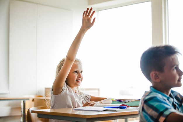 Girl sitting at table raising hand