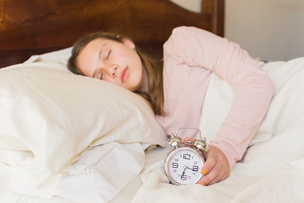 Girl sleeping with alarm clock on bed