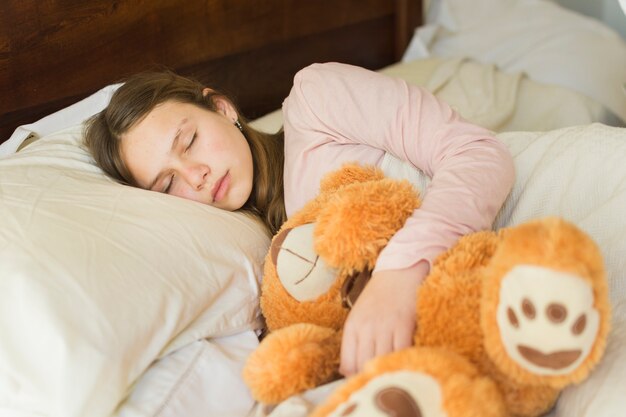 Girl sleeping with soft teddy bear on bed