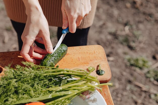 女の子はボード上の野菜をスライスし、自然にサラダを準備します。晴れた日と料理。クローズアップビュー。