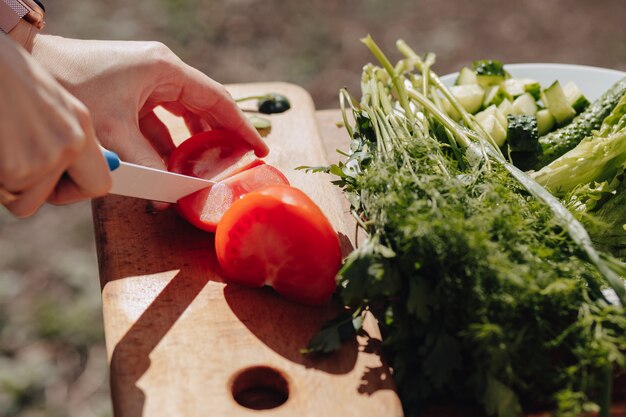 Girl slices vegetables on the board and prepares a salad on the nature. sunny day and cooking. close-up view.