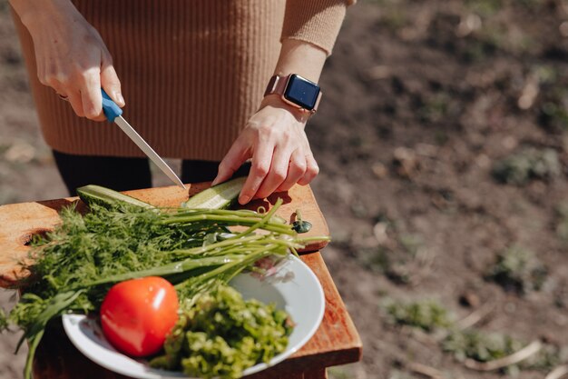 Girl slices vegetables on the board and prepares a salad on the nature. sunny day and cooking. close-up view.