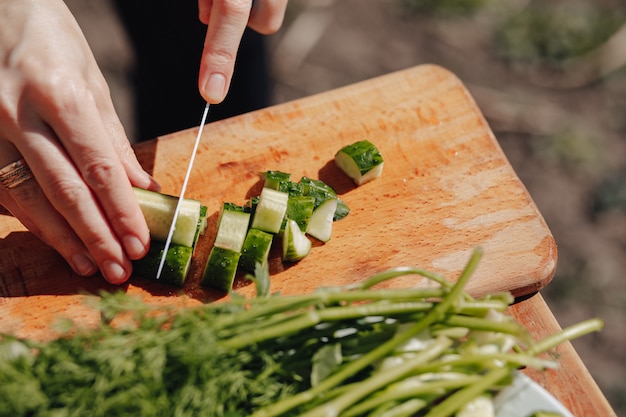 Girl slices vegetables on the board and prepares a salad on the nature. sunny day and cooking. close-up view.