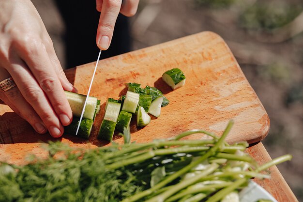 女の子はボード上の野菜をスライスし、自然にサラダを準備します。晴れた日と料理。クローズアップビュー。