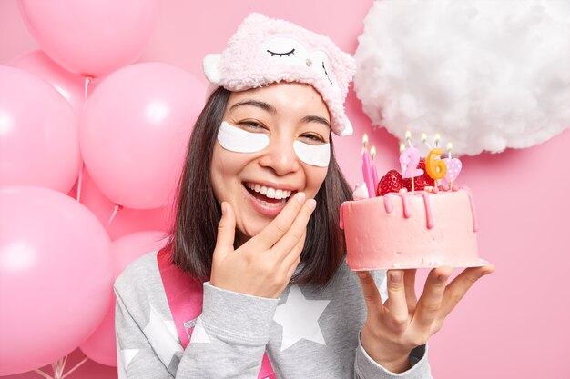 girl smiles broadly holds festive cake enjoys celebrating 26th bday at home undergoes beauty treatments before party wears sleepmask nightwear