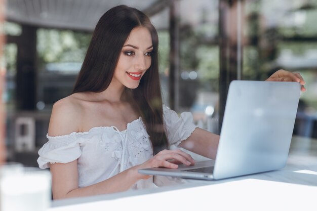 Girl smiling with red painted lips typing on a laptop