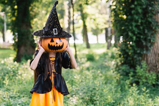 Girl in sorceress clothes closing face by pumpkin