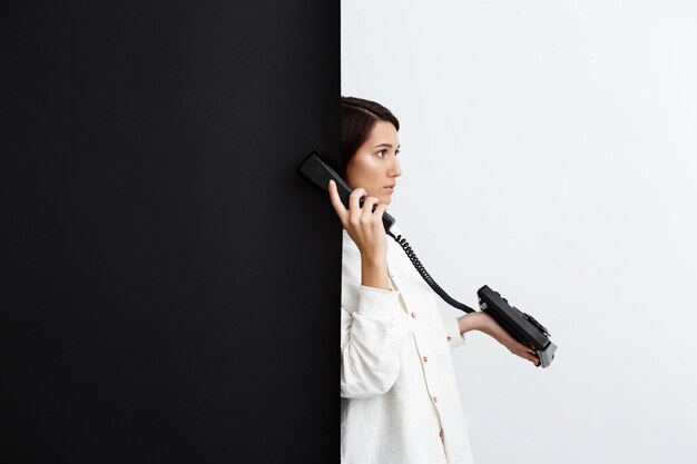 Girl speaking on old phone over black and white wall