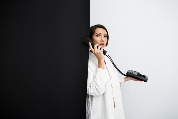 검은 색과 흰색 벽을 통해 오래 된 전화에 말하는 여자