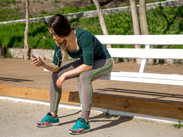 Girl in sports clothes sitting on the bench and listens to music, fitness ,sports motivation,sport,fitness