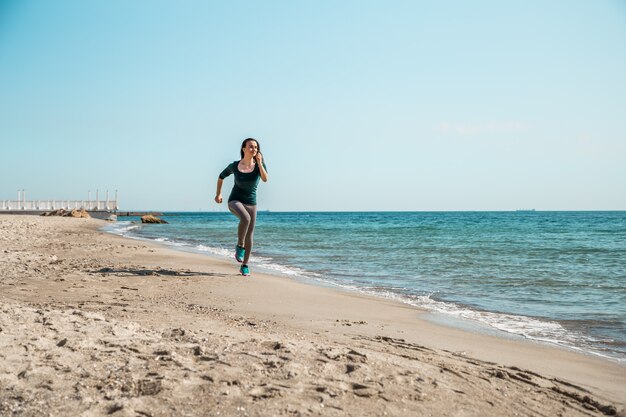 海に沿って実行しているスポーツウェアの女の子