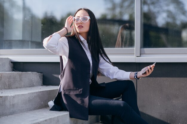 Girl on stairs with a mobile in hand and touching her glasses