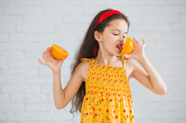 Девушка, стоящая на белом кирпичной стене, облизывая апельсины