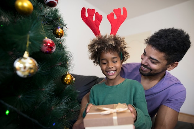 Free photo girl standing by christmas tree and unwrapping present box looking surprised