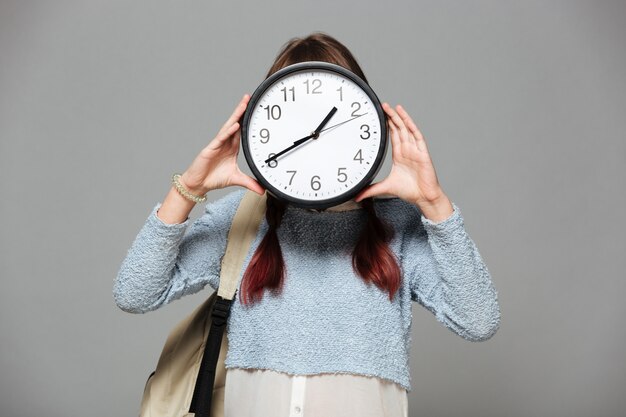 Girl standing covering face with clock