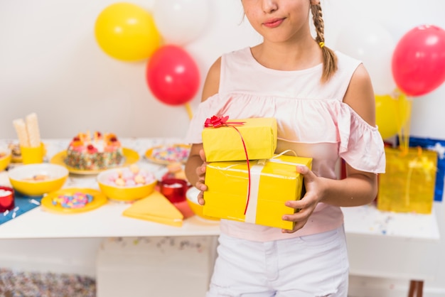 Девушка стоит перед столом с подарками в руке