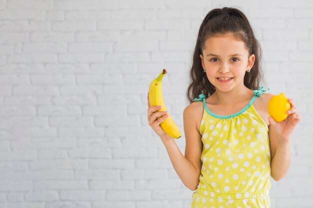 Girl standing in front of wall holding colorful ripe fruits