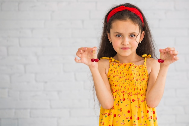 Girl standing in front of wall holding red cherries in her hand