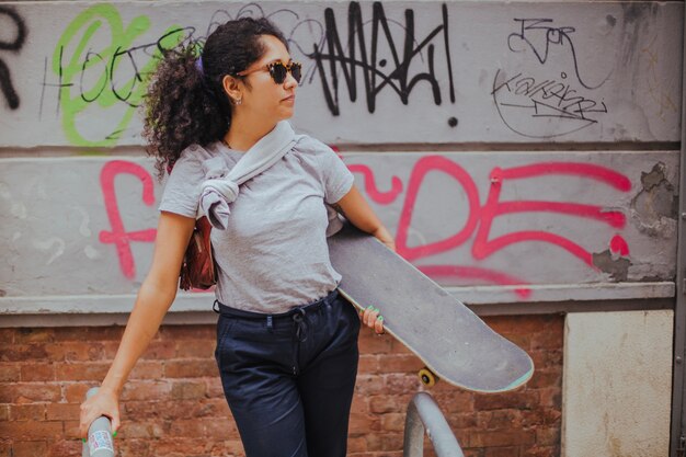 Girl standing outside holding skateboard leaning