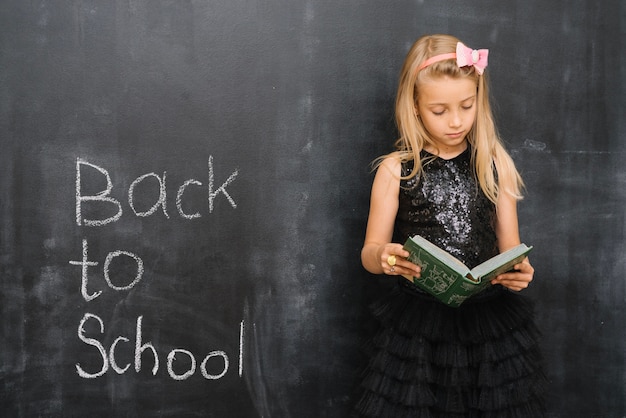 Girl standing and reading book at blackboard