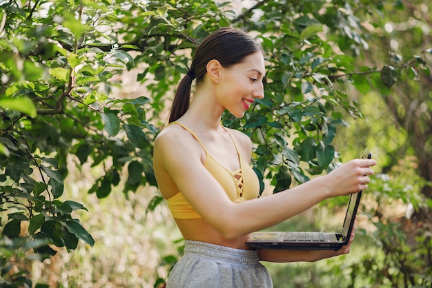Girl standing in a summer park and holding a laptop in her hands