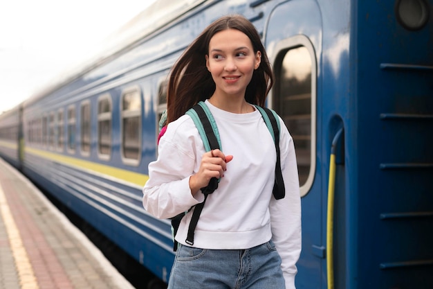 彼女のバックパックで電車の横に立っている女の子