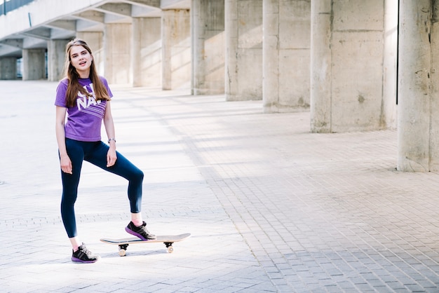 Бесплатное фото Девушка, стоящая с скейтбордом, глядя на камеру