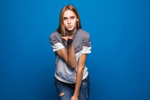 Girl stares in camera and blowing air kiss, isolated over blue background.