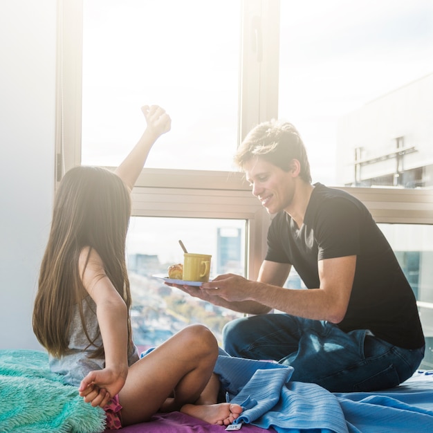 Girl stretching arm with her father holding breakfast