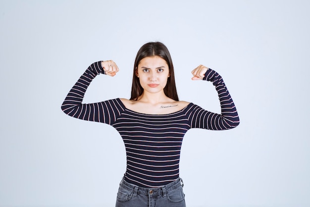 Ragazza in camicia a righe che dimostra i suoi muscoli del braccio.