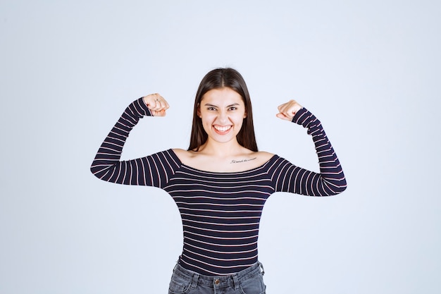 Girl in striped shirt demonstrating her arm muscles. 