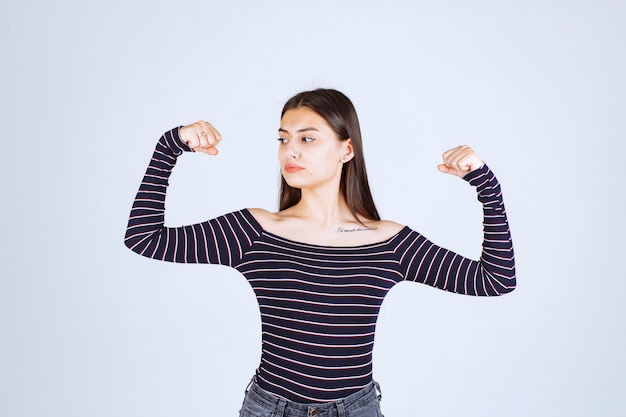 Девушка в полосатой рубашке демонстрирует мышцы рук.