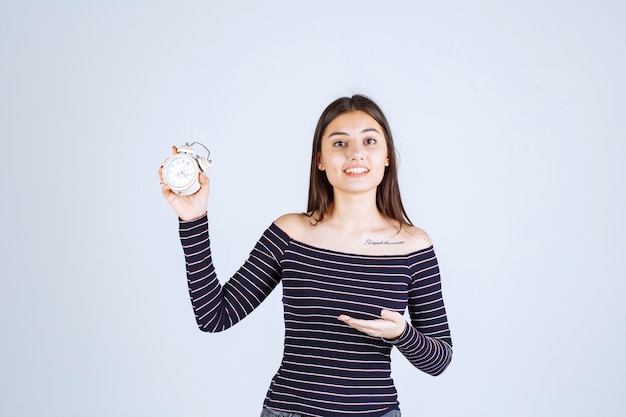Girl in striped shirt holding an alarm clock and promoting it as a new product.