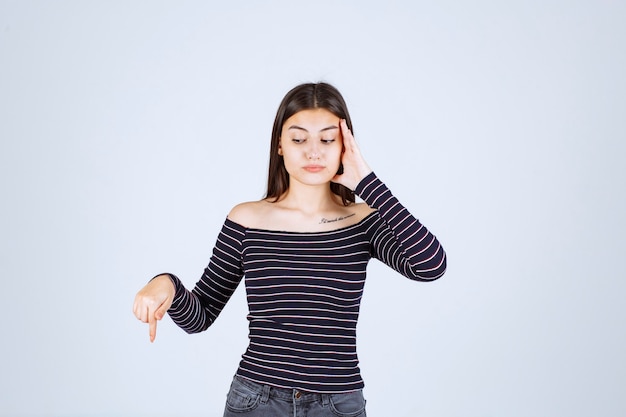 Девушка в полосатой рубашке держится за голову, когда она устала или у нее болит голова.