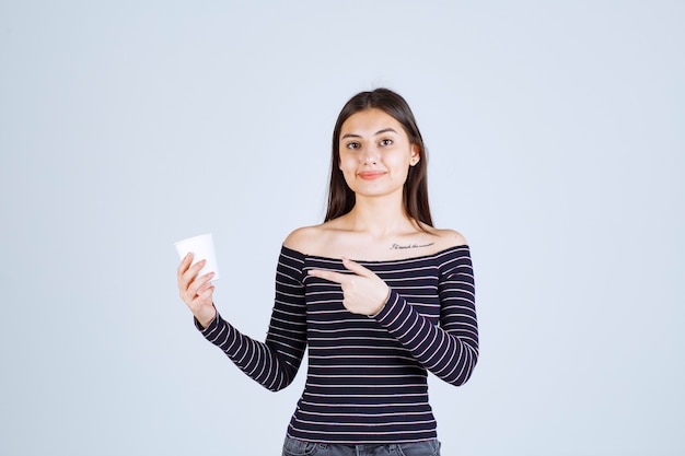 Girl in striped shirt holding a plastic coffee cup and introducing it as a product.