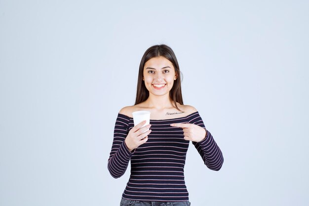 プラスチック製のコーヒーカップを持って、それを製品として紹介する縞模様のシャツの女の子。