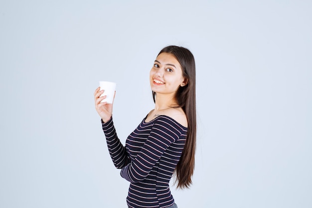 Girl in striped shirt holding a plastic coffee cup and looks positive.