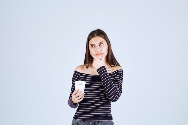 Girl in striped shirt holding a plastic coffee cup and thinking.