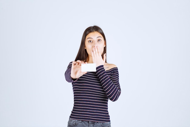 Girl in striped shirt holds a business card and looks surprized. 