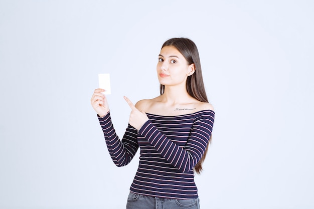 Девушка в полосатой рубашке держит визитку и указывает на нее.