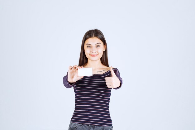 Girl in striped shirt holds a business card and showing thumb up sign. 