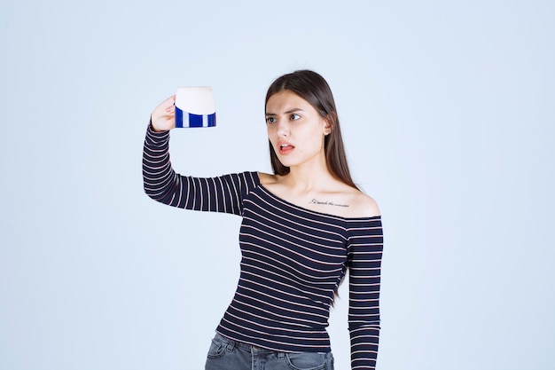 Girl in striped shirt looks at the coffee mug and feels dissatisfied