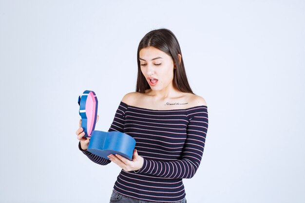 Girl in striped shirt opens a blue gift box and gets surprized. 