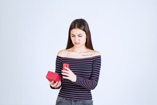 Girl in striped shirt opens a red gift box and gets confused. 