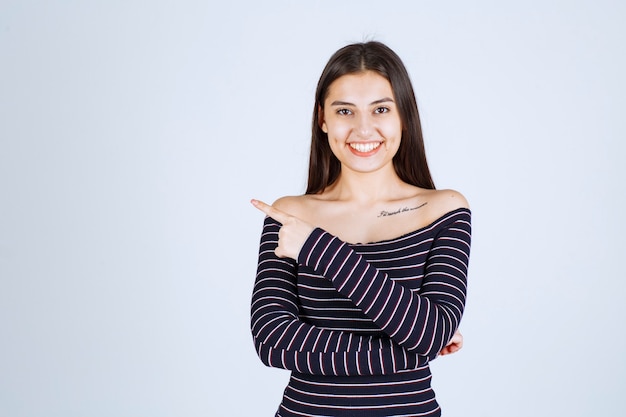 Girl in striped shirt pointing at somebody on the left side. 