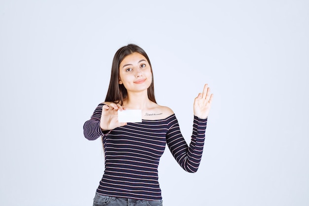 Ragazza in camicia a righe che presenta il suo biglietto da visita con fiducia.