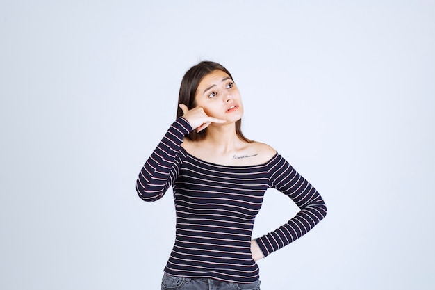 Ragazza in camicia a righe che mostra il segnale di chiamata.