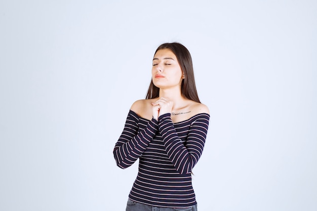 Ragazza in camicia a righe che unisce le sue mani e che prega.