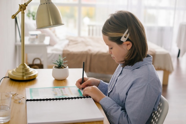 机に座ってメモを書く家で勉強している女の子。ホームスクーリング、遠隔教育の概念